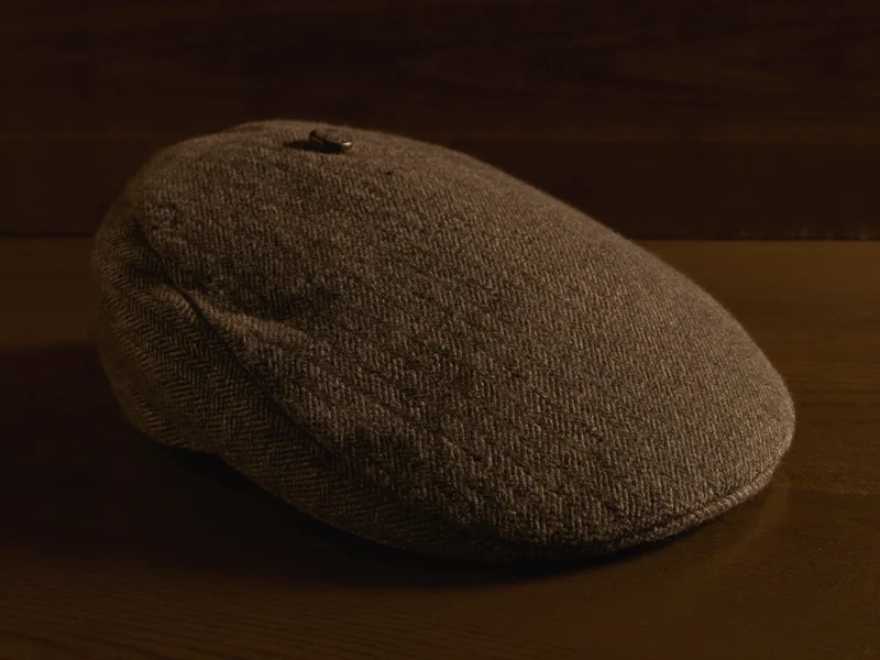Hnědá tvídová plochá čepice na tmavém dubovém stole